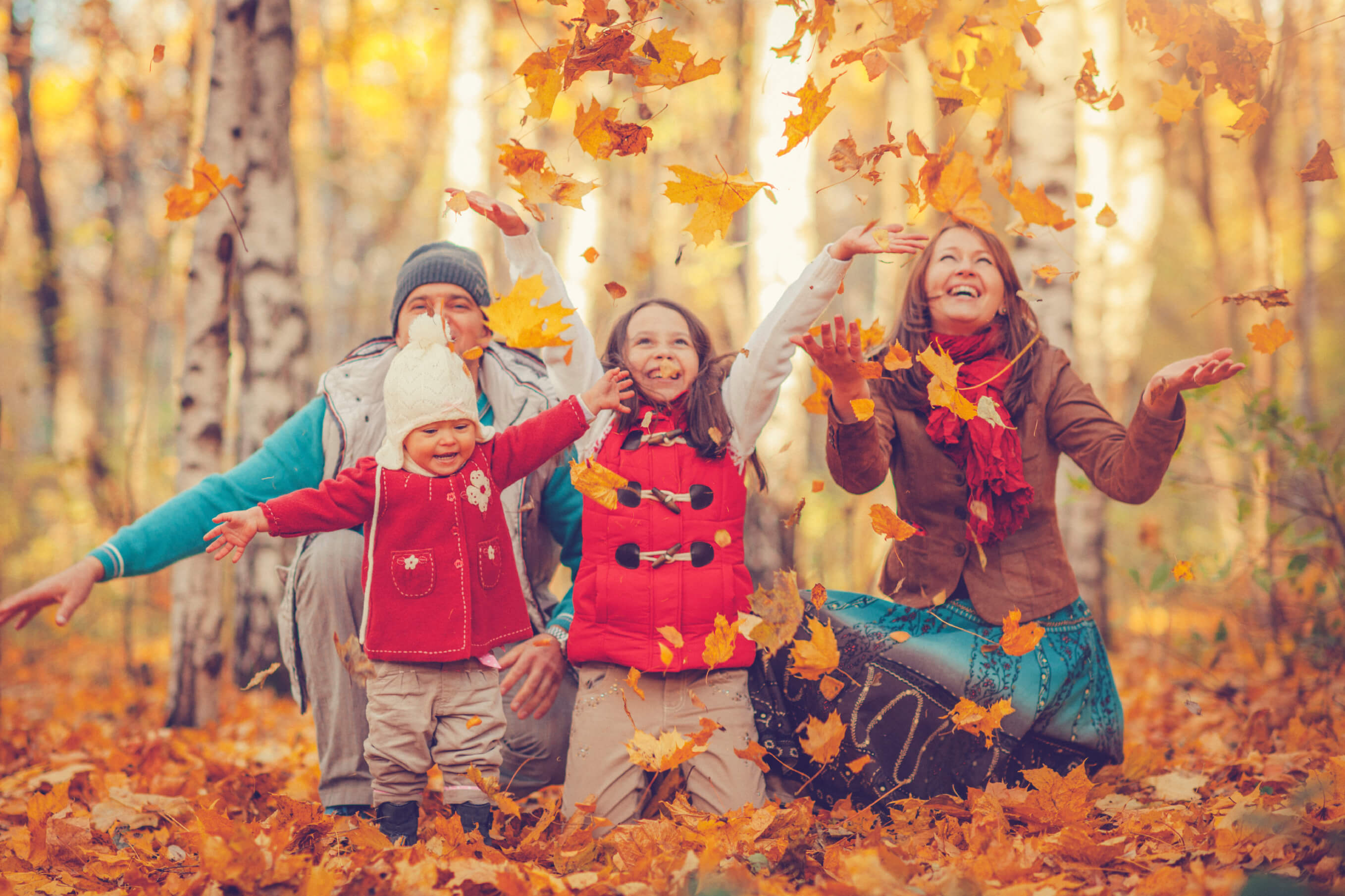 Family outside during the fall season throwing leaves in the air. Thanksgiving Survival Guide for Working Parents